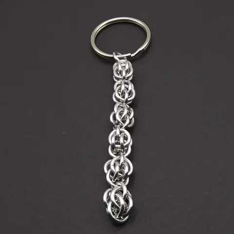 Silver chain mail keychain with large keyring laying on a dark grey background.