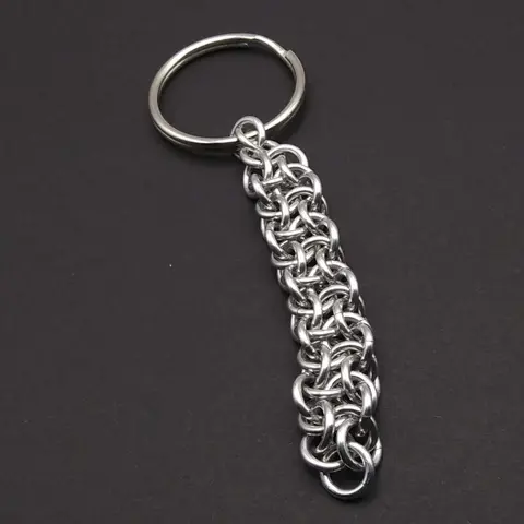 Silver chain mail keychain with large keyring laying on a dark grey background.