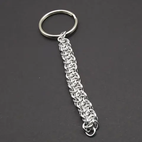 Silver chain mail keychain with large keyring laying on a dark grey background.