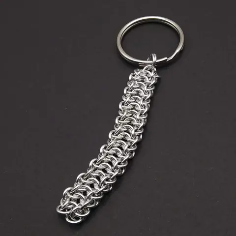 Silver chain mail keychain with large keyring laying on a dark grey background.