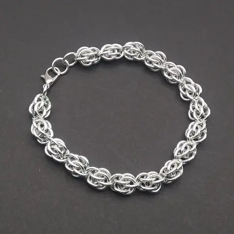 Silver chain mail bracelet laying on a dark grey background