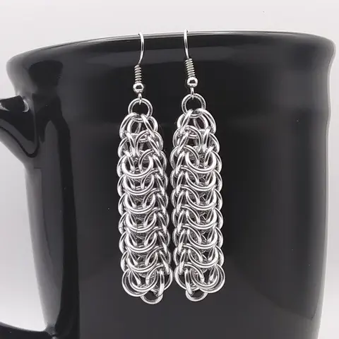 Silver dangly chain mail earrings hanging on a black mug.