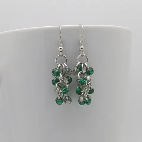 Silver dangly earrings with clear and emerald beads hanging on a white mug.