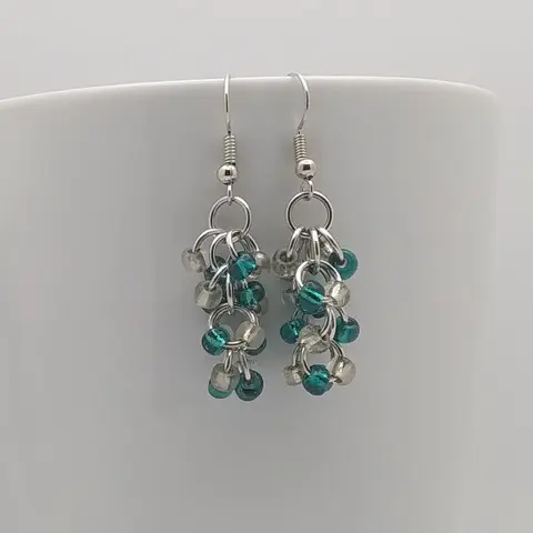 Silver dangly earrings with clear and teal beads hanging on a white mug.