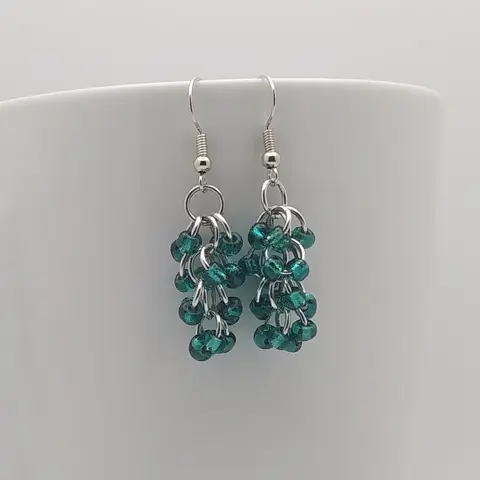 Silver dangly earrings with silver-lined teal beads hanging on a white mug.