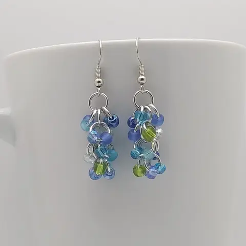 Silver dangly earrings with turquoise mix beads hanging on a white mug.