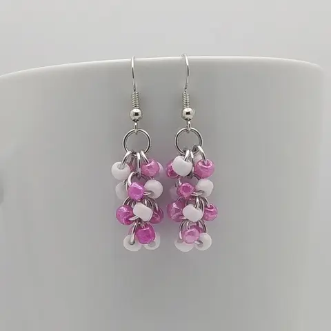 Silver dangly earrings with white and rose beads hanging on a white mug.