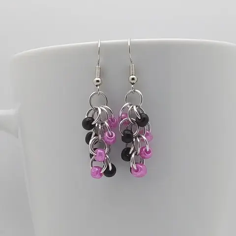 Silver dangly earrings with black and dark pink beads hanging on a white mug.