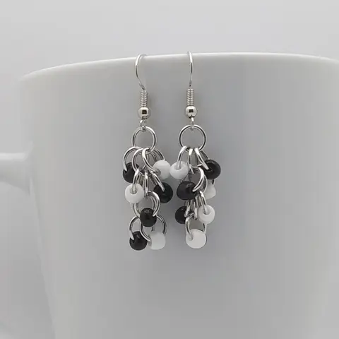 Silver dangly earrings with black and white beads hanging on a white mug.