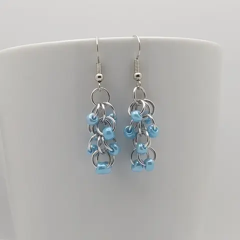 Silver dangly earrings with blue beads hanging on a white mug.