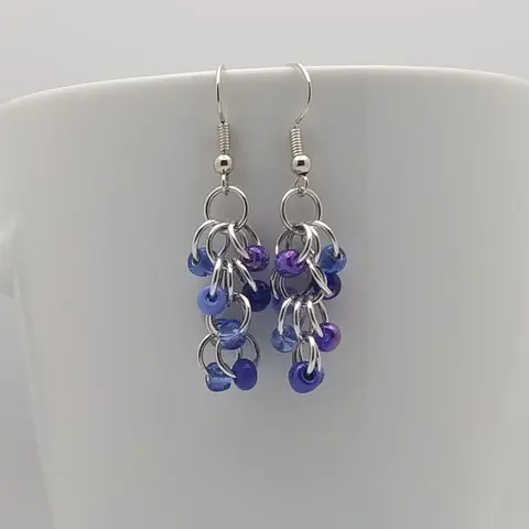 Silver dangly earrings with sapphire blue mix beads hanging on a white mug.