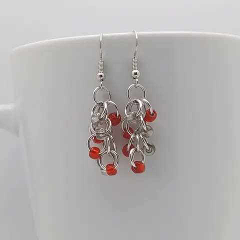 Silver dangly earrings with clear and red beads hanging on a white mug.