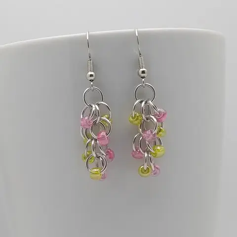 Silver dangly earrings with pink and yellow beads hanging on a white mug.