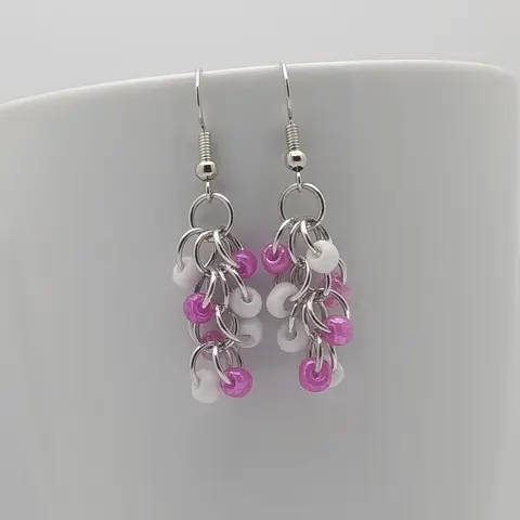 Silver dangly earrings with white and pink beads hanging on a white mug.