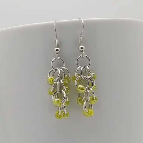 Silver dangly earrings with yellow beads hanging on a white mug.