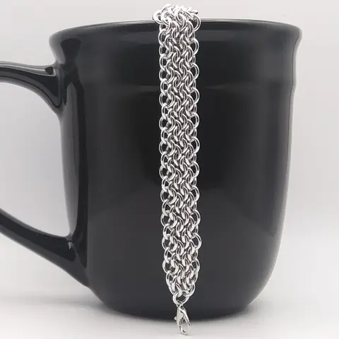 Bright silver aluminum chain mail bracelet on a black mug.