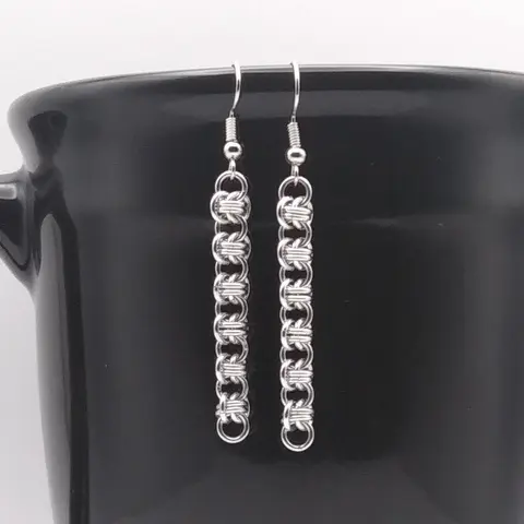 Bright silver aluminum chain mail earrings on a black mug.