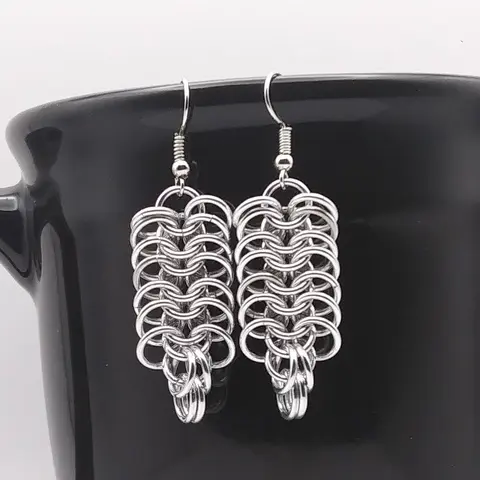 Bright silver aluminum chain mail earrings on a black mug.