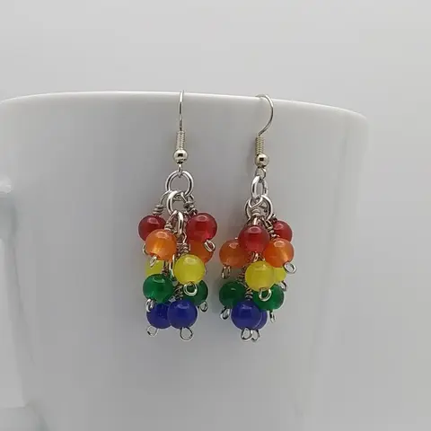 Bright silver aluminum chain mail earrings with rainbow wrapped glass beads on a white mug.