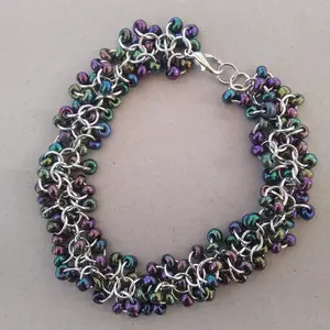 Bright silver aluminum chain mail bracelet with dark rainbow beads on a light grey background.