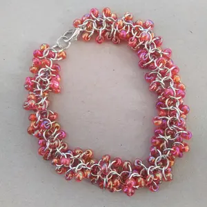 Bright silver aluminum chain mail bracelet with red rainbow beads on a light grey background.