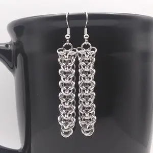 Bright silver aluminum chain mail earrings on a black mug.