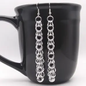 Extra long bright silver aluminum chain mail earrings on a black mug.