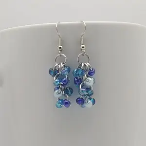 Bright silver aluminum chain mail earrings with blue mix beads on a white mug.