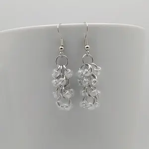 Bright silver aluminum chain mail earrings with clear beads on a white mug.