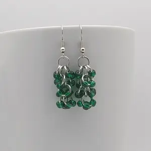 Bright silver aluminum chain mail earrings with silver-lined emerald beads on a white mug.