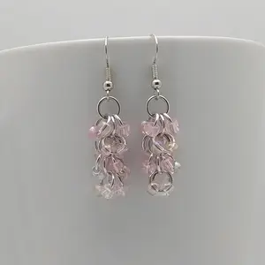 Bright silver aluminum chain mail earrings with pink mist beads on a white mug.