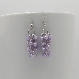 Bright silver aluminum chain mail earrings with purple beads on a white mug.