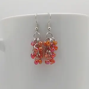 Bright silver aluminum chain mail earrings with red rainbow beads on a white mug.