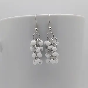 Bright silver aluminum chain mail earrings with white beads on a white mug.