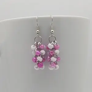 Bright silver aluminum chain mail earrings with white and rose beads on a white mug.