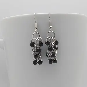 Bright silver aluminum long chain mail earrings with black beads on a white mug.