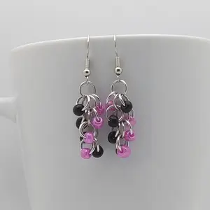 Bright silver aluminum chain mail earrings with black and rose beads on a white mug.