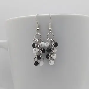 Bright silver aluminum chain mail earrings with black and white beads on a white mug.