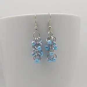 Bright silver aluminum chain mail earrings with blue beads on a white mug.