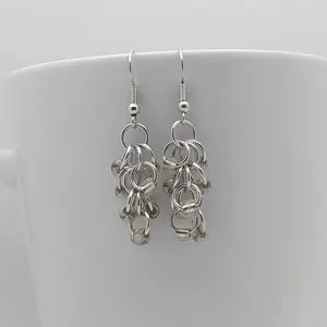 Bright silver aluminum chain mail earrings with silver-lined clear beads on a white mug.