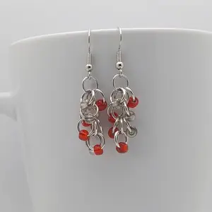 Bright silver aluminum chain mail earrings with clear and red beads on a white mug.