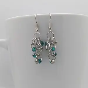 Bright silver aluminum chain mail earrings with clear and teal beads on a white mug.