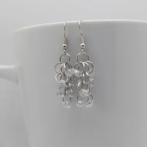 Bright silver aluminum chain mail earrings with crystal luster beads on a white mug.