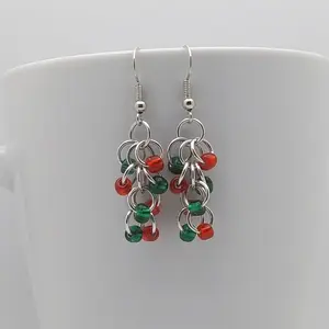 Bright silver aluminum chain mail earrings with emerald and red beads on a white mug.