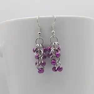 Bright silver aluminum chain mail earrings with metallic violet beads on a white mug.