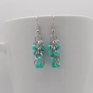 Bright silver aluminum chain mail earrings with opaque turquoise beads on a white mug.