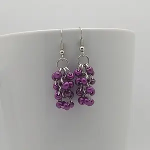 Bright silver aluminum chain mail earrings with metallic violet beads on a white mug.