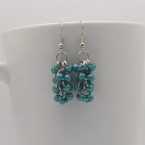 Bright silver aluminum chain mail earrings with metallic teal beads on a white mug.