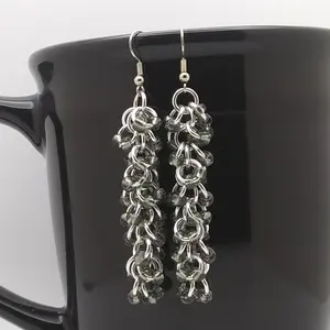 Bright silver aluminum long chain mail earrings with silver-lined grey beads on a black mug.