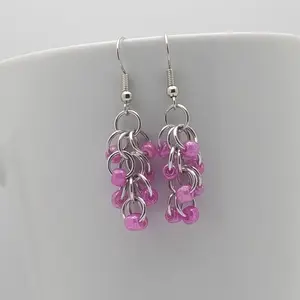 Bright silver aluminum long chain mail earrings with rose beads on a white mug.